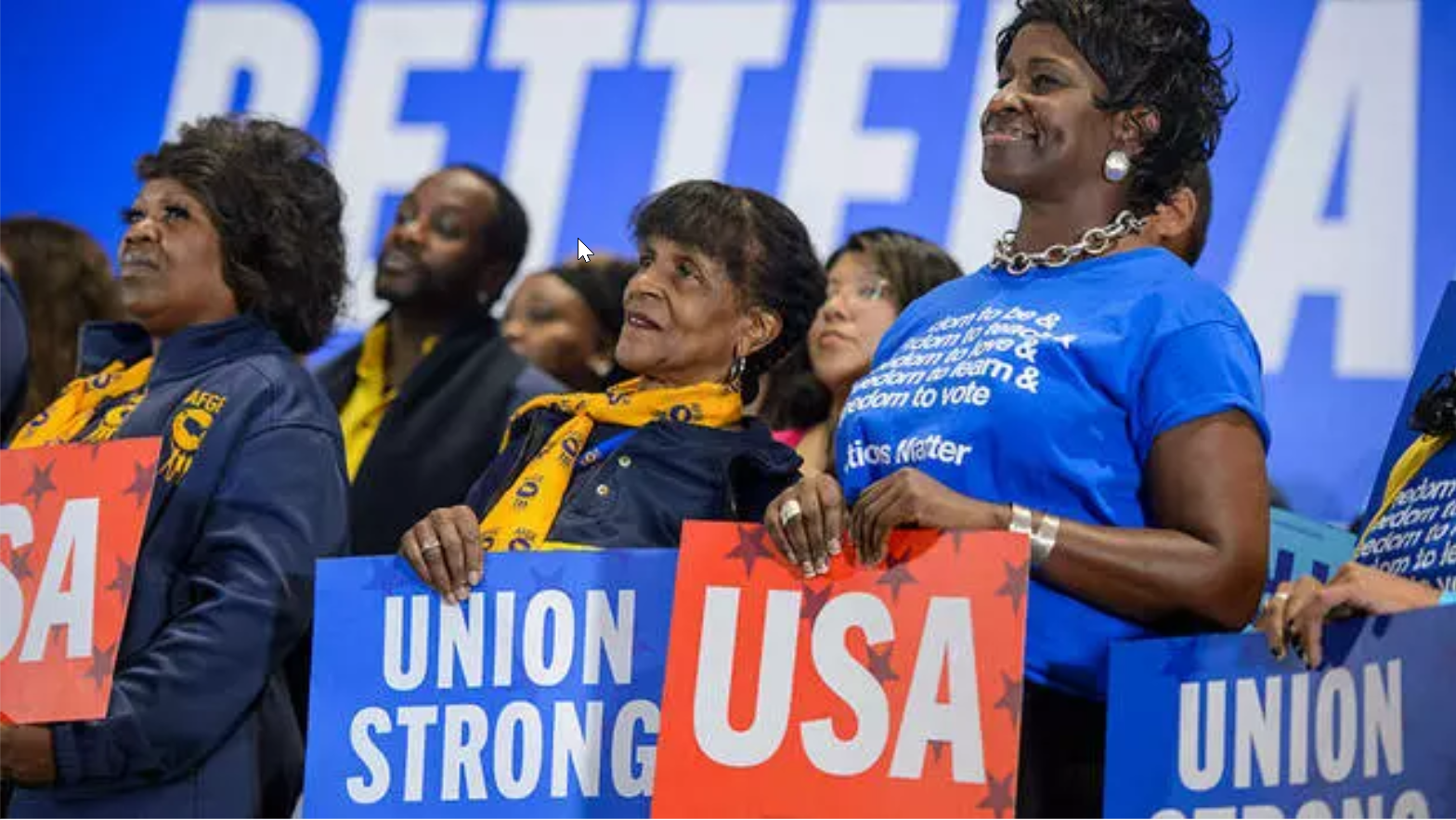 Union members look on during a rally for the midterm elections. They are holding signs that say "USA" and "Union strong."