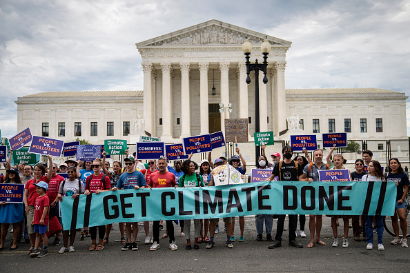 A group of environmental activists rally in front of the U.S. Supreme Court holding a banner that says: Get Climate Done.